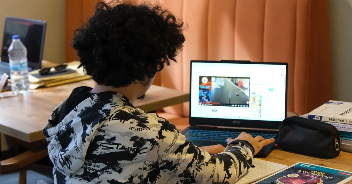 Adolescent utilisant un ordinateur portable pour apprendre à la maison, entouré de matériel d'étude et de livres.