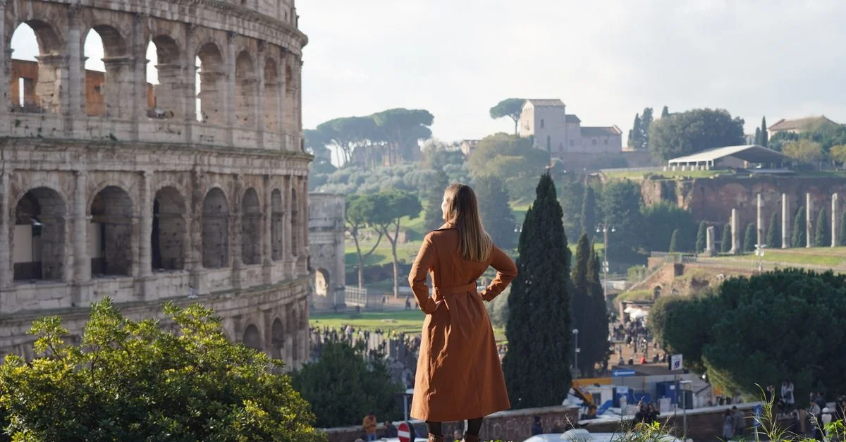 Une femme en manteau regarde le Colisée à Rome par une journée claire.