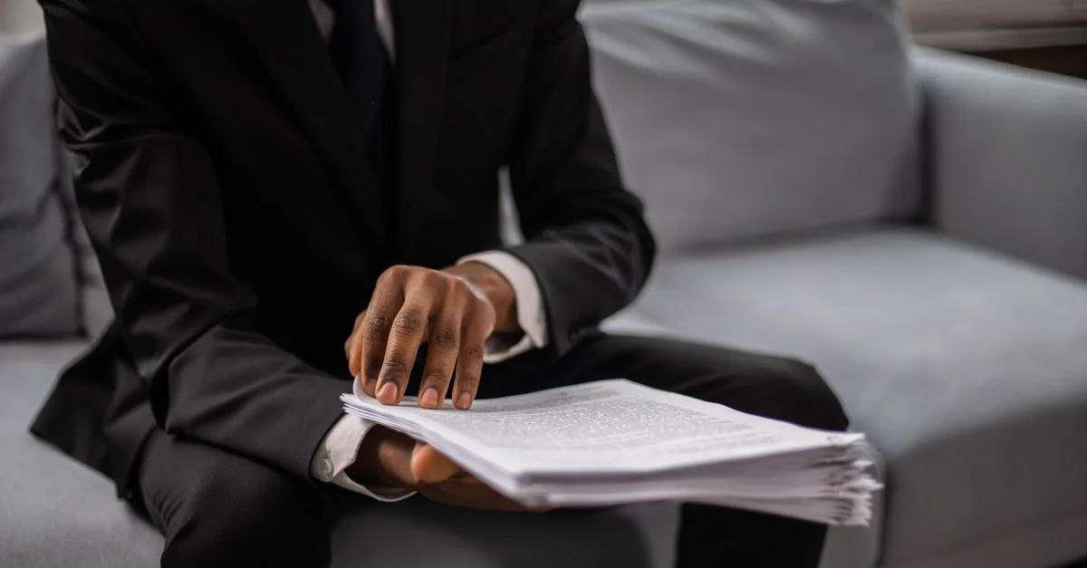 Gros plan d'un homme d'affaires en costume examinant des documents assis sur un canapé à l'intérieur.