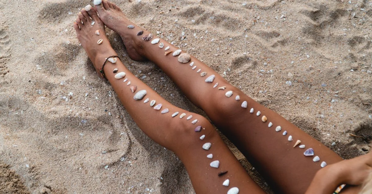 Une scène de plage sereine mettant en vedette les jambes d'une femme ornées de coquillages, sur des rivages sablonneux.