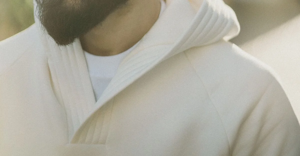 Gros plan sur un homme barbu en hoodie blanc capturé sous une lumière douce. Mettant en avant un style décontracté.