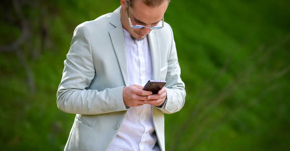 Un homme en costume vert menthe utilise son smartphone en extérieur, illustrant un style de vie et une mode modernes.