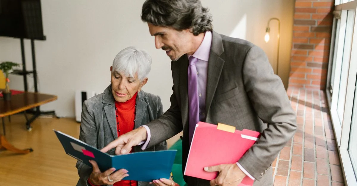 Une femme et un homme d'affaires seniors discutent de documents dans un bureau moderne baigné de lumière naturelle.