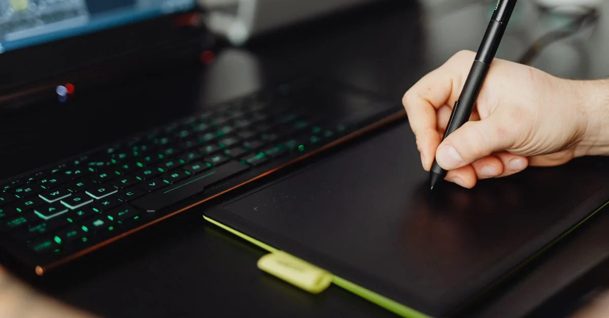 Gros plan d'une main utilisant un stylet sur une tablette graphique dans un espace de travail moderne.