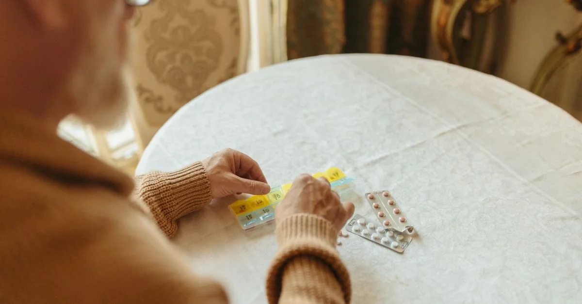 Personne âgée triant les médicaments quotidiens avec un organisateur de pilules sur une table à l'intérieur.