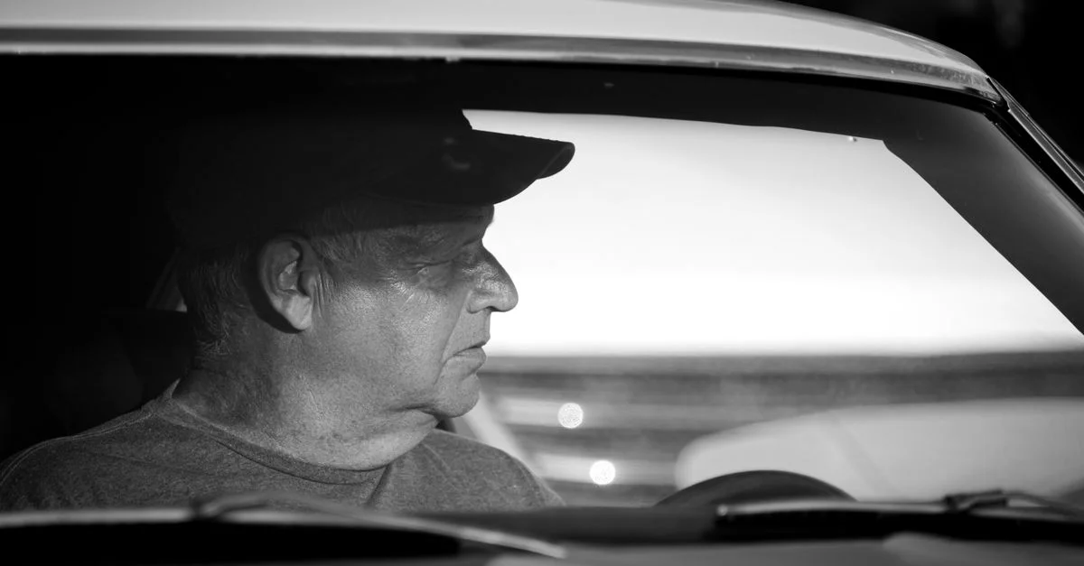Profil d'un homme conduisant une voiture en noir et blanc, capturant un moment de réflexion.